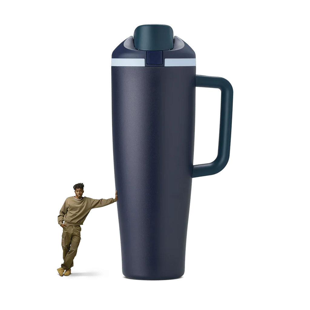 Large navy blue 40oz travel tumbler with handle, shown oversized next to standing person